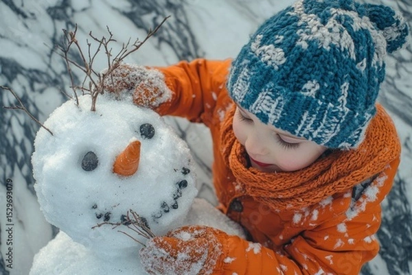Fototapeta A child in orange winter clothes carefully decorates a snowman with twigs, adding the finishing touches to its cheerful face.