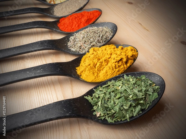 Fototapeta Assorted colorful spices in black spoons on wooden background