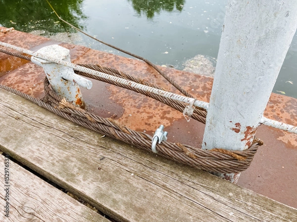 Obraz A weathered and rustic dock hardware piece featuring twisted rope laid upon aged wooden planks, capturing a sense of calm and tranquility in a serene coastal environment by the water