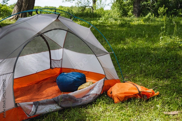 Obraz Experience the joy of setting up a cozy camping tent nestled harmoniously in a lush, vibrant green landscape, surrounded by the serenity of nature and a picturesque scenery that invites adventure