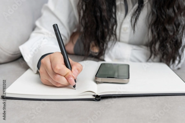 Fototapeta Notebook planner being used for organizing tasks while a smartphone rests nearby