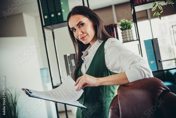 Fototapeta Confident businesswoman holding documents in an elegant office setting, embodying professionalism and success