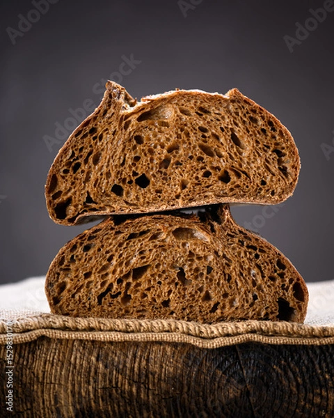 Obraz Two half of rye sourdough bread in section on a rustic wooden board. Artisan farmhouse-style loaf captured in warm natural lighting