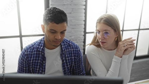Fototapeta Man and woman collaborating in a modern office, focusing on a computer screen and discussing work, highlighting teamwork, professional attire, and an interior workplace setting.