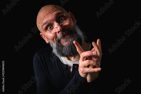 Obraz Portrait of a cunning-looking bald man with gray beard and glasses, clasping hands. Dark background. Mischievous or scheming expression. Concept of plotting, sarcasm, or ironic humor