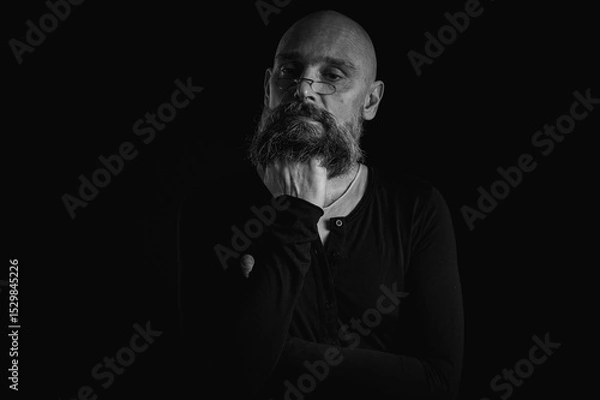 Obraz Black and white portrait, pensive bald man with beard and glasses looking up, touching temple, deep in thought, isolated on black background. Concept of ideas, planning, decision making