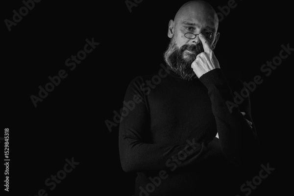 Obraz Black and white portrait, pensive bald man with beard and glasses looking up, touching temple, deep in thought, isolated on black background. Concept of ideas, planning, decision making