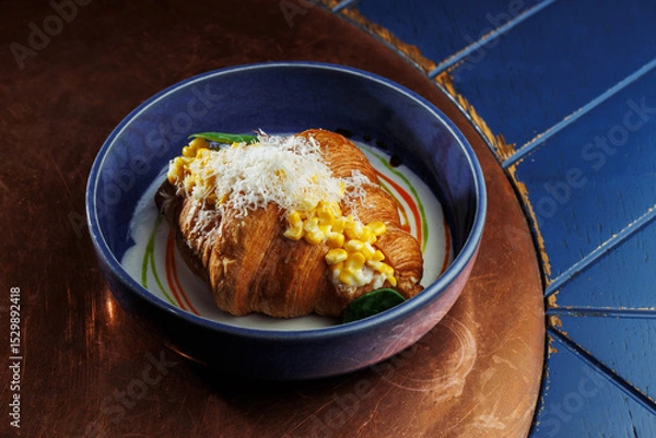 Fototapeta Gourmet croissant with creamy corn filling and parmesan cheese in blue bowl – elegant food presentation on rustic copper background
