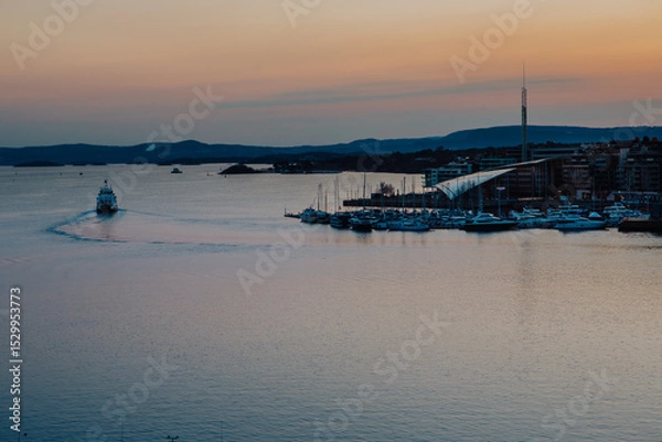Fototapeta A vibrant sunset bathes the Astrup Fearnley Museum of Modern Art in Oslo, with a ferry gracefully sailing by, creating a harmonious blend of art, architecture, and the beauty of the Oslofjord
