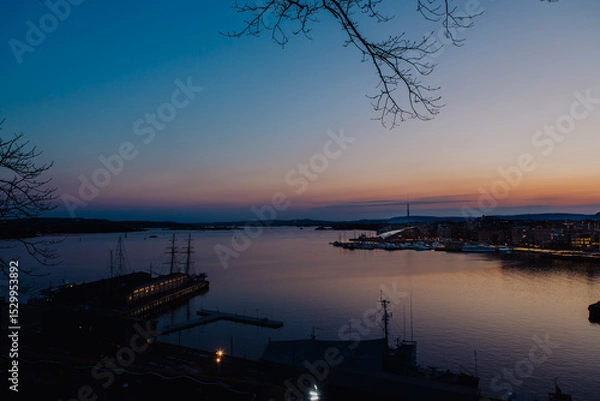 Fototapeta A vibrant sunset bathes the Astrup Fearnley Museum of Modern Art in Oslo, with a ferry gracefully sailing by, creating a harmonious blend of art, architecture, and the beauty of the Oslofjord