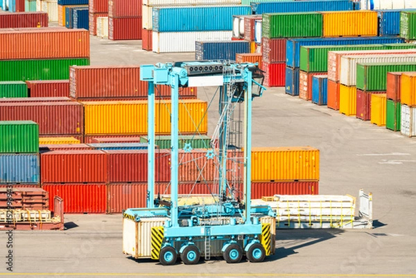 Obraz Container handler vehicle in cargo terminal with stacked multicolored cargo containers