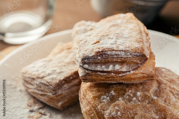 Fototapeta Puff pastry dusted with powdered sugar in a white plate, macro shot
