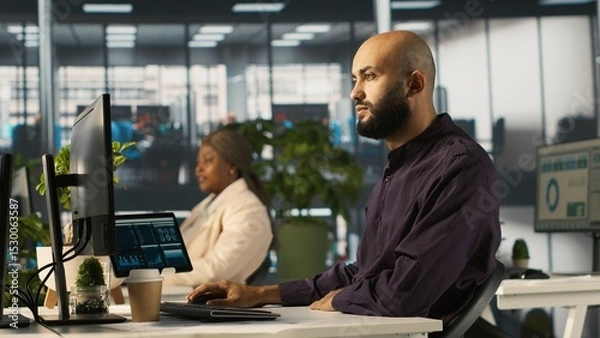 Obraz Arab man in office reviewing financial graphs, analyzing key performance indicators. Middle Eastern employee in workspace looking over data trends and strategic insights, camera A