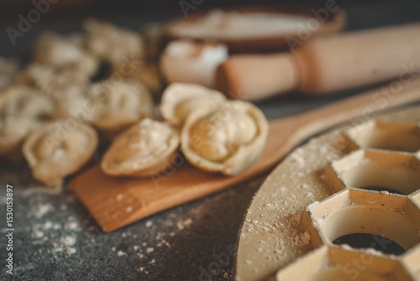 Obraz Close-up of raw dumplings on a floured surface with a metal mold and rolling pin in the background, capturing the rustic process of homemade cooking