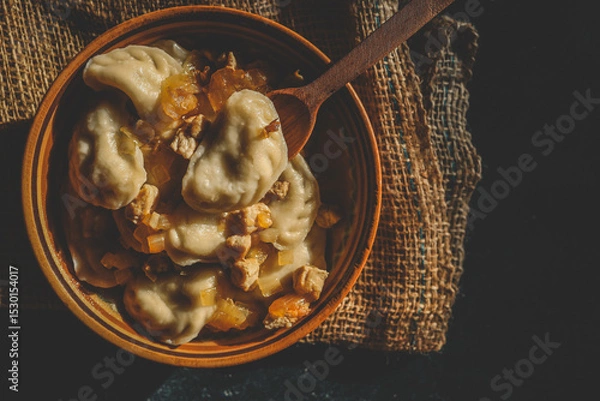 Obraz Top view of traditional dumplings served with fried onions and meat in rustic ceramic bowls, placed on burlap and a wooden board