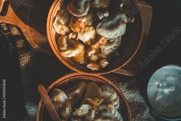 Obraz Top view of traditional dumplings served with fried onions and meat in rustic ceramic bowls, placed on burlap and a wooden board