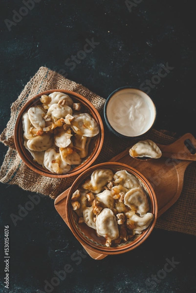 Obraz Top view of traditional dumplings served with fried onions and meat in rustic ceramic bowls, placed on burlap and a wooden board