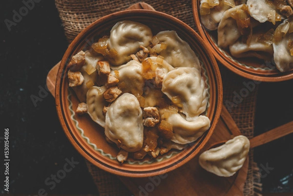 Obraz Rustic presentation of dumplings with fried onions and meat in ceramic bowls, served on burlap with one dumpling on a wooden spoon in the foreground