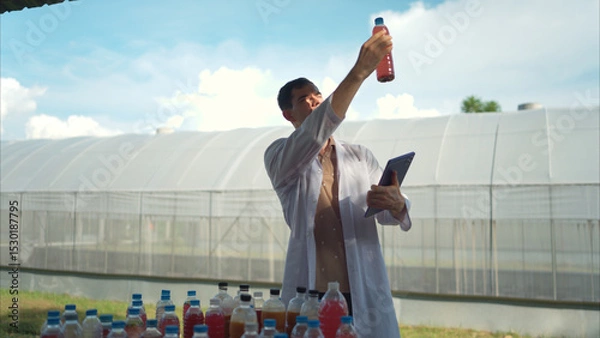 Fototapeta A researcher in a lab coat uses a tablet to inspect colorful liquid samples