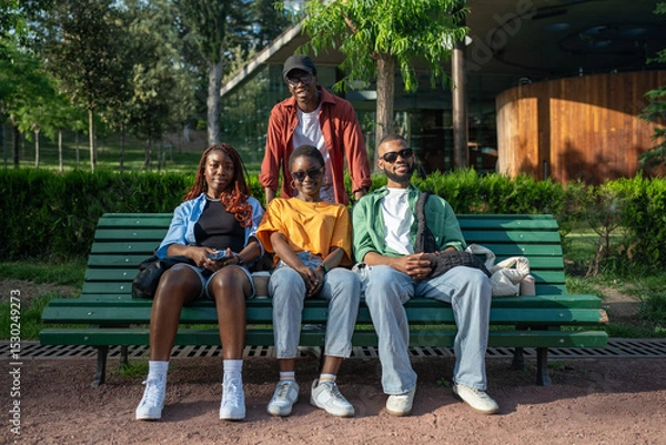 Fototapeta Portrait of four happy black best friends relaxing and hugging on park bench, enjoying of meeting, look at camera. Close friendship, share joyful moments together on stroll, rest and relax after work