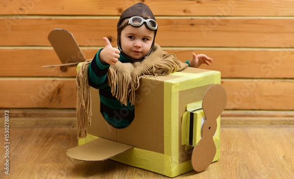 Fototapeta Flying child flying with cardboard wings. Kid dreams of pilot. Baby fly with paper plane. Boy in aviator helmet indoors. Child flying with toy airplane. Dreaming kid Flying in cardboard box.