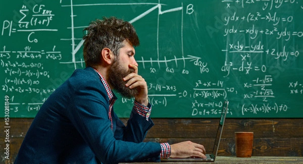 Fototapeta Teacher explains math at blackboard. Professor in classroom with chalkboard. University professor writes math formula. Bearded teacher. Professor teaching lesson in classroom. Professor explains math.