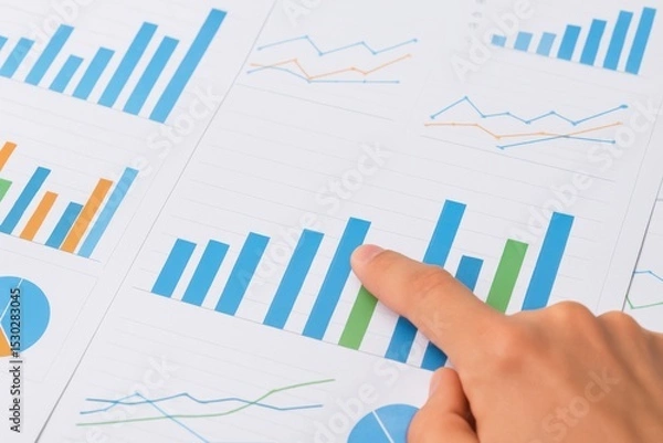 Obraz Detailed analysis of financial data shown in graphs and charts with a hand pointing at a blue bar representing growth in an office setting.