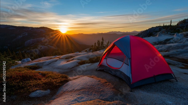 Fototapeta A red camping tent set up on rocky terrain during sunset, with vibrant sun rays shining over the landscape.