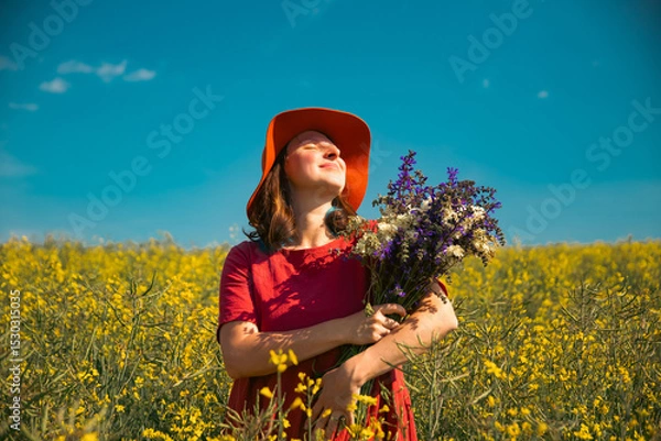 Obraz Trendy woman with stylish hat feeling free in the field with flowers
