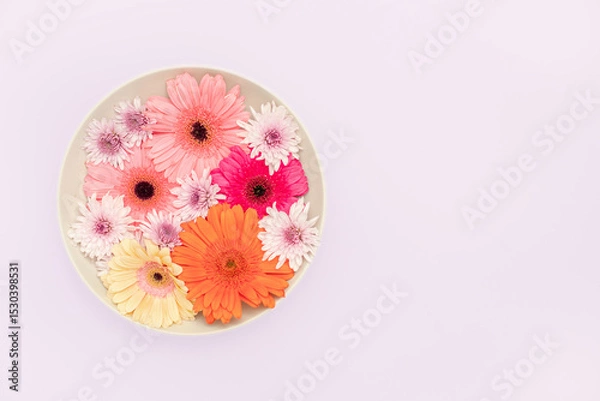 Obraz Top-down view of a vibrant floral composition with orange, pink, white, and magenta flowers, including mums and gerberas, arranged in a light beige ceramic plate with a space for text lilac background