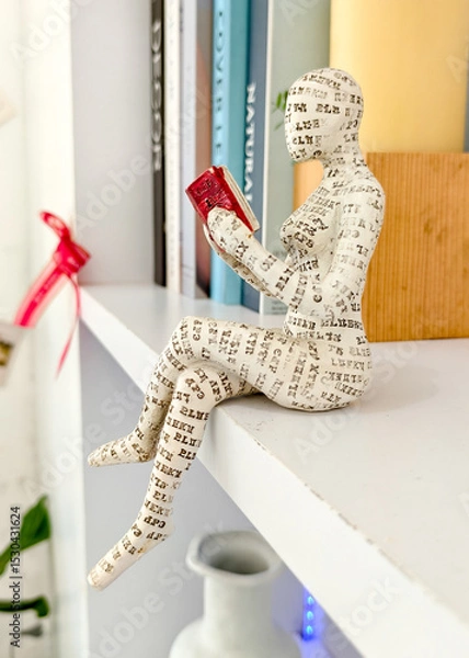 Fototapeta Bookworm Sculpture: A unique, artistic sculpture of a person engrossed in reading a book sits on a shelf, capturing the essence of leisure and the joy of reading.