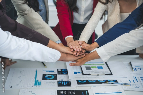 Fototapeta Business people joining hands over a table with financial charts, showing teamwork and collaboration