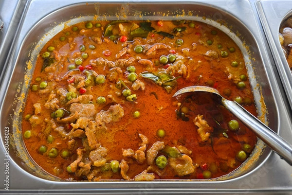 Fototapeta Thai-style pork curry served in a stainless steel tray, featuring rich red curry sauce with sliced pork, pea eggplants, chili, and kaffir lime leaves.