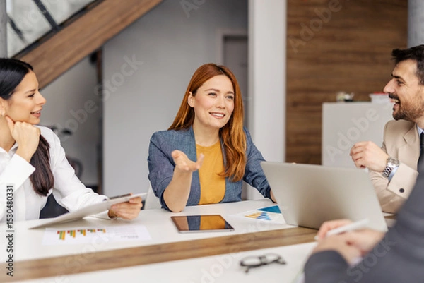 Fototapeta Portrait of smiling businesswoman sitting at conference table in gender balanced collective and discussing project.