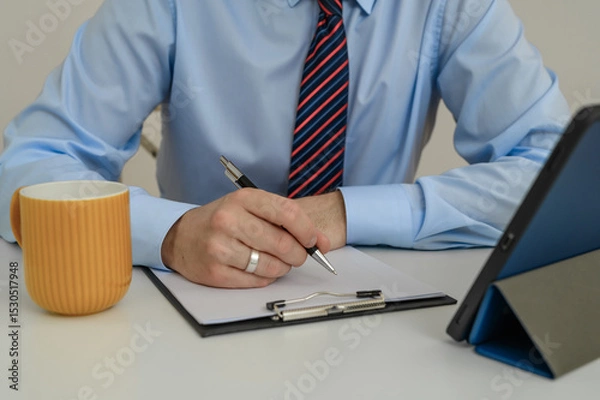 Obraz A man in an office sitting at his desk at work filling out paperwork
