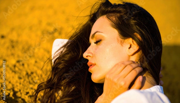 Fototapeta Closeup shot captures woman face illuminated by warm yellow glow, showcasing her serene expression against textured background. image evokes sense of tranquility and beauty