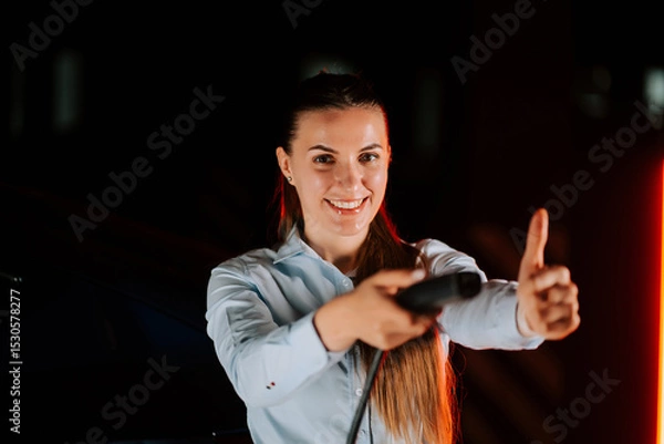 Obraz Woman charges electric car in underground parking lot while smiling and giving thumbs up