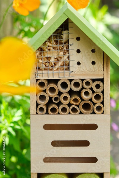 Fototapeta An insect hotel or bee hotel in a summer garden with orange flowers. An insect hotel is a manmade structure created to provide shelter for insects in a variety of shapes and sizes and materials.	