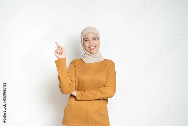 Fototapeta Confident Woman Pointing Upwards in Casual Attire isolated on a White Background