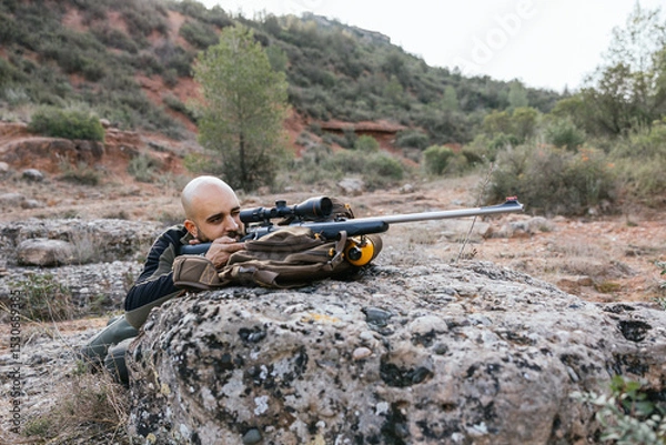 Fototapeta Hunter taking aim with rifle in natural landscape