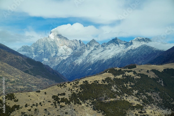 Fototapeta Mount Siguniang (Four Sisters Mountain) in Sichuan, China. The prominent snow-covered peak, The foreground features brown hills contrasting with alpine backdrop and a wide, vivid blue sky 