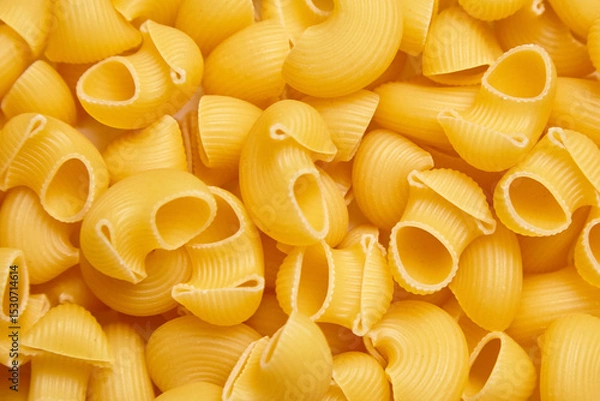 Fototapeta Detailed close-up of uncooked pipe rigate pasta showcasing its curved, ribbed structure and golden color, ideal for food textures or culinary backgrounds