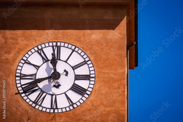 Obraz Detail of antique tower clock on textured orange wall against deep blue sky in Italy