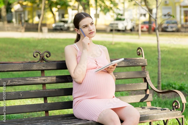 Fototapeta pregnant woman sits on a park bench and writes a to do list to the hospital