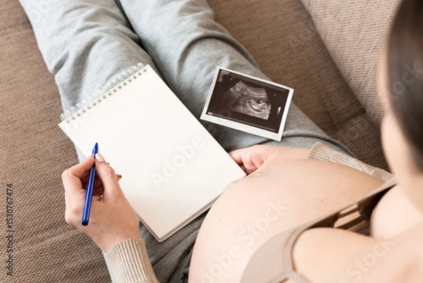 Fototapeta Top view caring future mother writing diary with ultrasound. pregnant woman tummy making notes feeling during pregnancy or creating scrapbook
