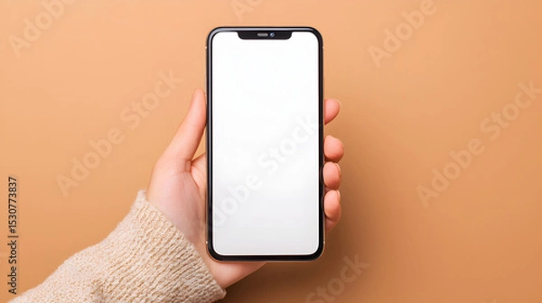 Obraz A hand holds a smartphone with a blank white screen against a peach background.