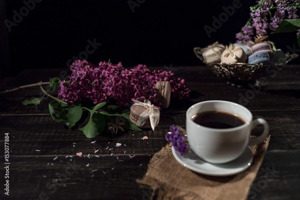 Obraz Cup of coffee on linen napkin and several macarons in braid vase with branch of lilac.