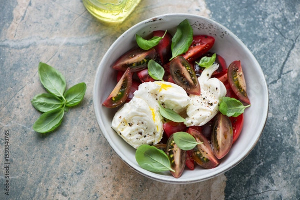Fototapeta Caprese with heirloom tomatoes and torn buffalo mozzarella, horizontal shot on a beige and grey granite background, high angle view