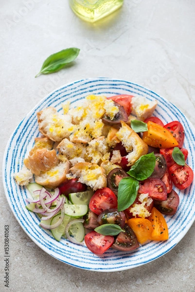 Fototapeta Blue and white plate with panzanella or italian tomato and bread salad, vertical shot on a beige stone background, high angle view