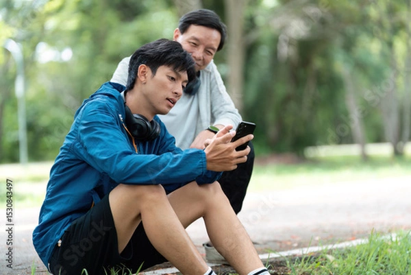 Fototapeta Father and Son Relaxing After Exercise. Sharing moments and technology.